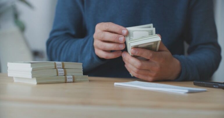 Entrepreneur managing financial transactions with cash bundles on desk