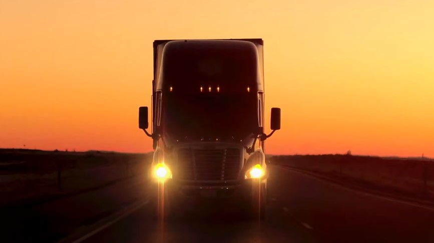 A semi-truck navigates a highway at sunrise